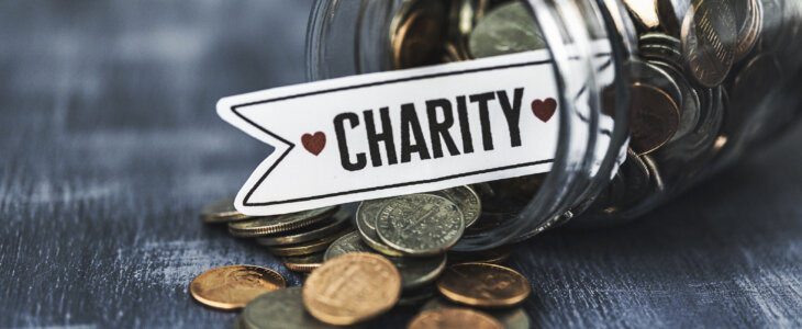 Glass jar filled with American coins with blue background and copy space. SIgn with money reads: CHARITY