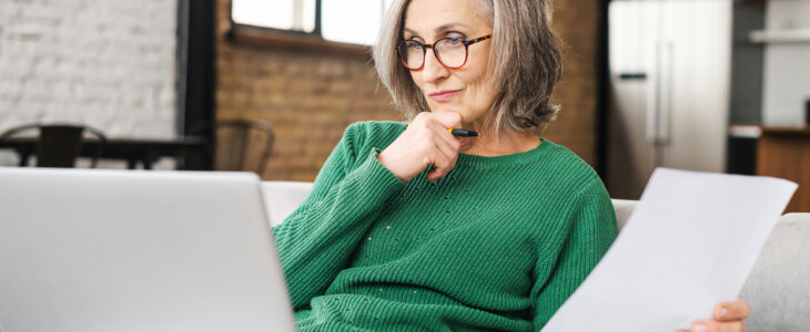 Senior woman wearing green sweater looking at retirement accounts on her laptop